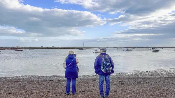 Walkers beside the Orford Estuary on the Suffolk Coast Path, with boats moored on the River Ore.