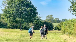 Walkers on the Cotswold Way National Trail crossing open countryside in the Cotswolds, England.
