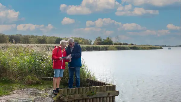 Walkers reading a map beside a river with reedbeds and open water in the Norfolk Broads.