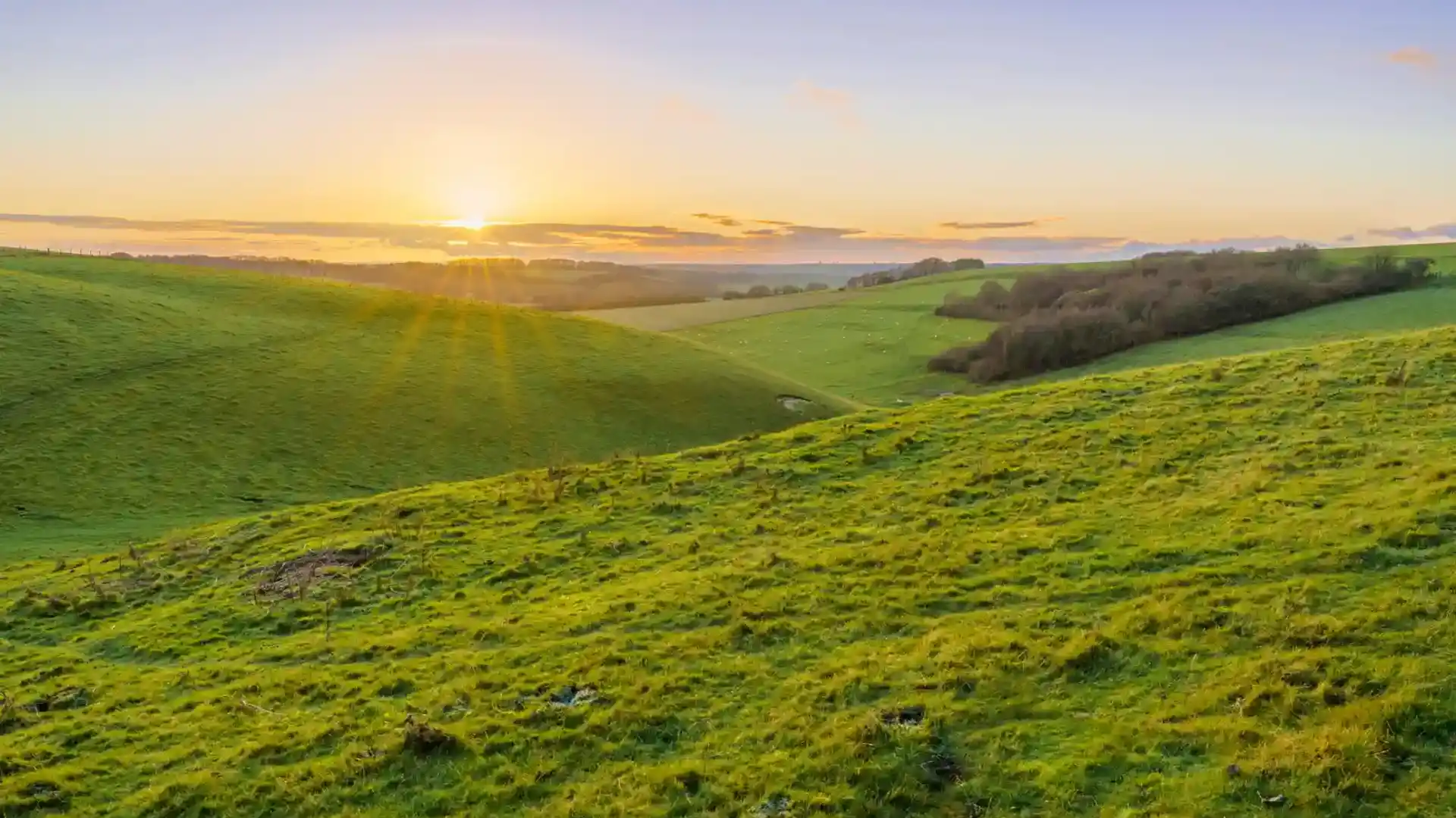 A golden sunset, low illuminated cloud on the horizon over a deep green grass valley, North Wessex Downs AONB.