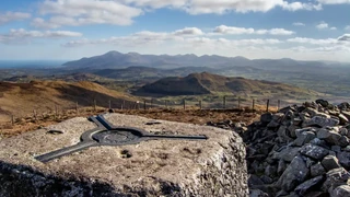 Summit view across the Mourne Mountains in County Down, Northern Ireland, with granite peaks, rolling farmland, and the Irish Sea on the horizon.