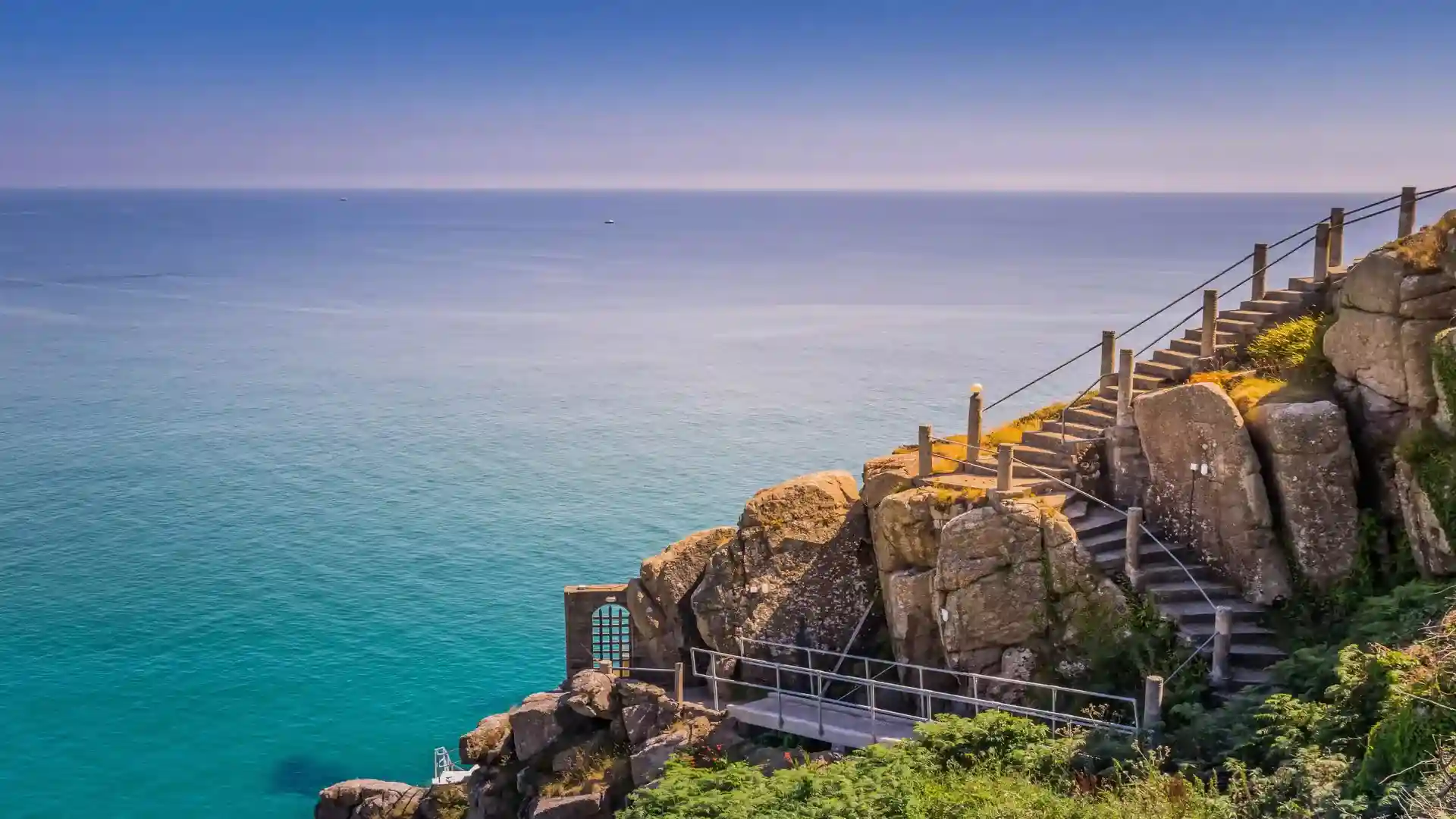 Stone steps and clifftop path on the South West Coast Path above the Atlantic Ocean in Cornwall, with turquoise sea and exposed rocky headland.