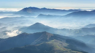 Layered mountain ridges and forested hills in Urkiola Natural Park, Basque Country, with mist drifting through valleys and rolling upland terrain.