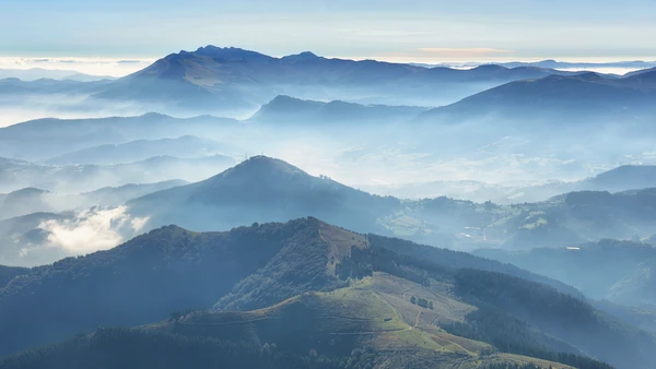 Layered mountain ridges and forested hills in Urkiola Natural Park, Basque Country, with mist drifting through valleys and rolling upland terrain.