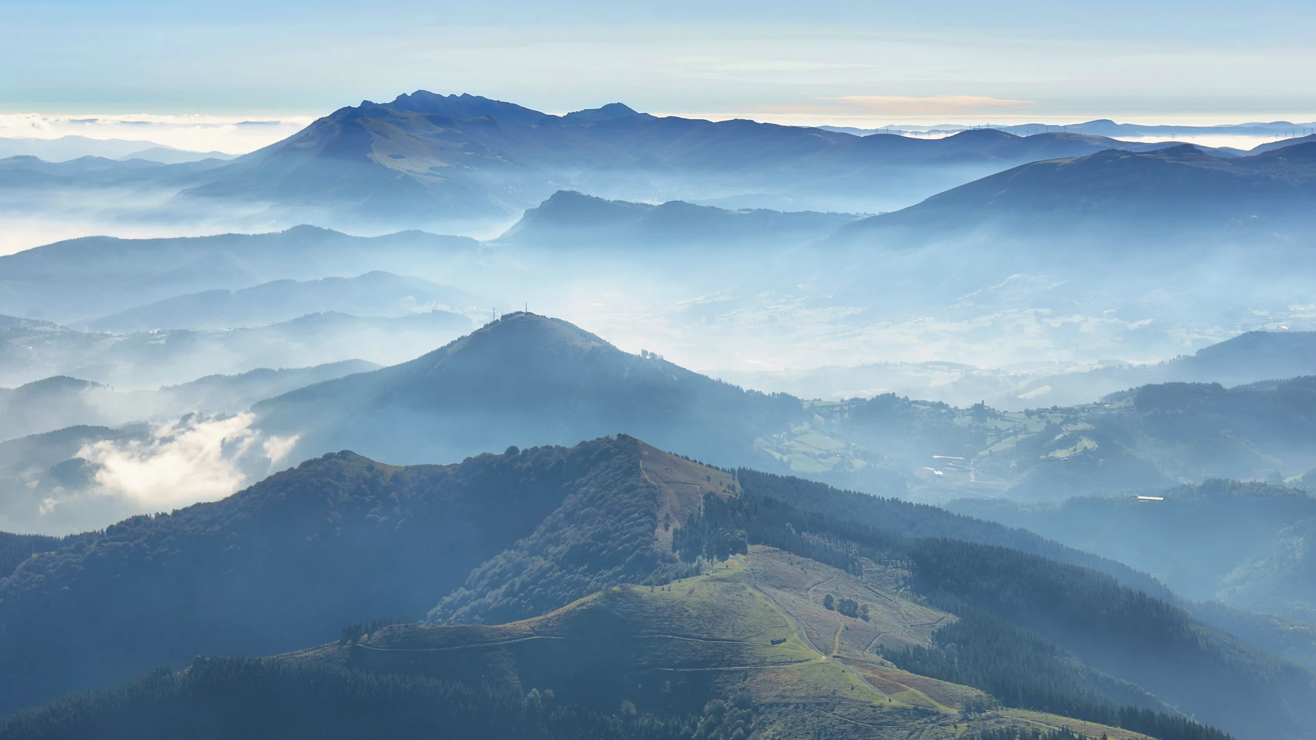 Layered mountain ridges and forested hills in Urkiola Natural Park, Basque Country, with mist drifting through valleys and rolling upland terrain.