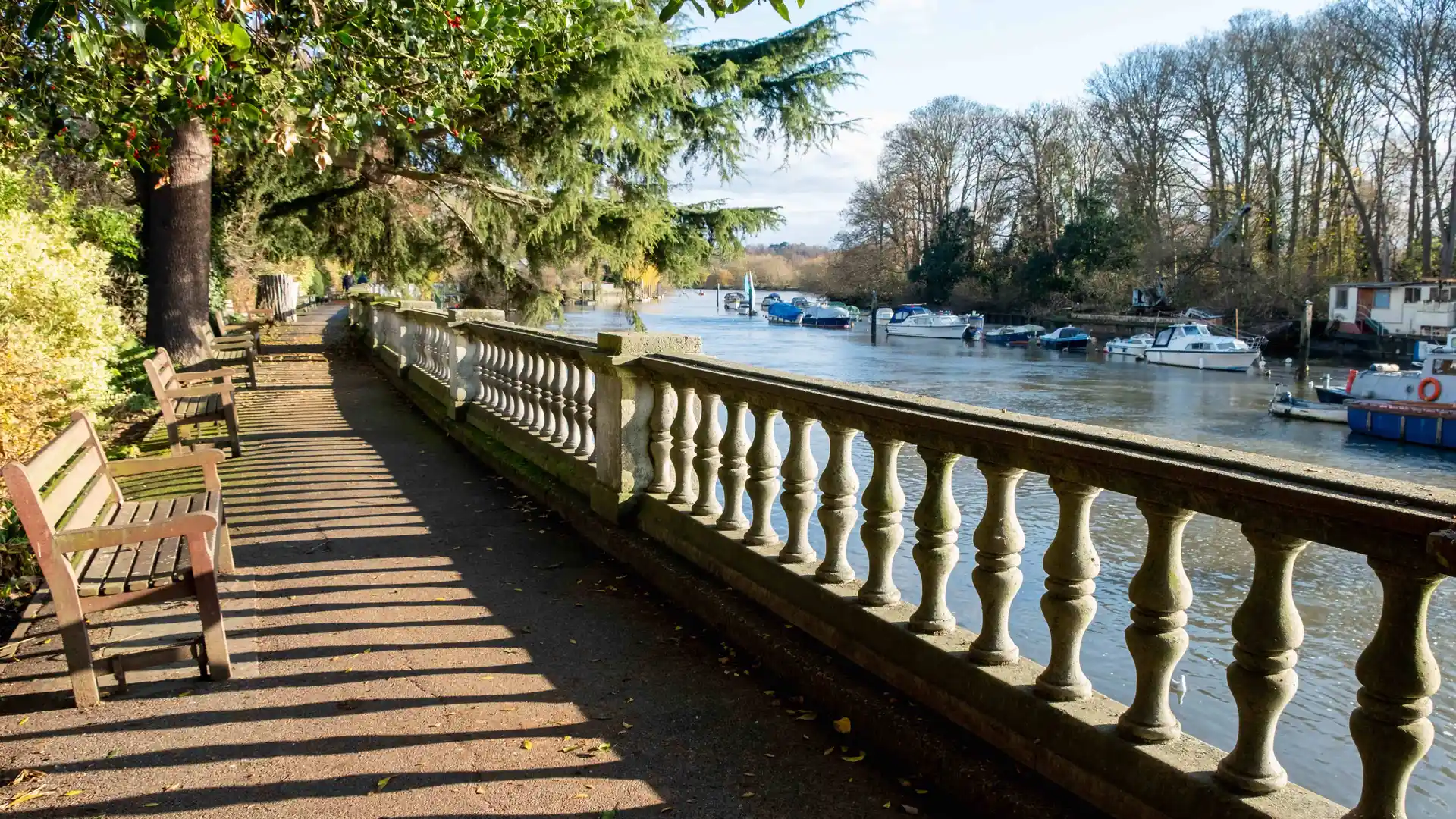 Riverside walkway with benches and moored boats along the Thames Path in London.