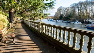 Riverside walkway with benches and moored boats along the Thames Path in London.
