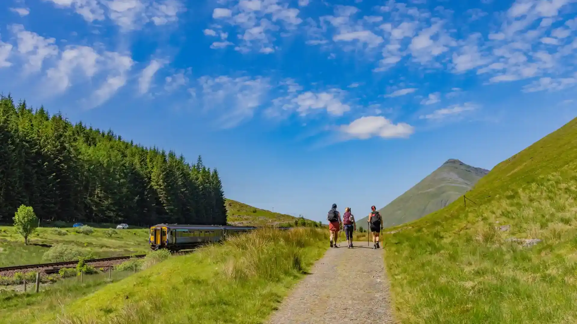 Walkers on the West Highland Way with train and Buachaille Etive Mòr in the Scottish Highlands.