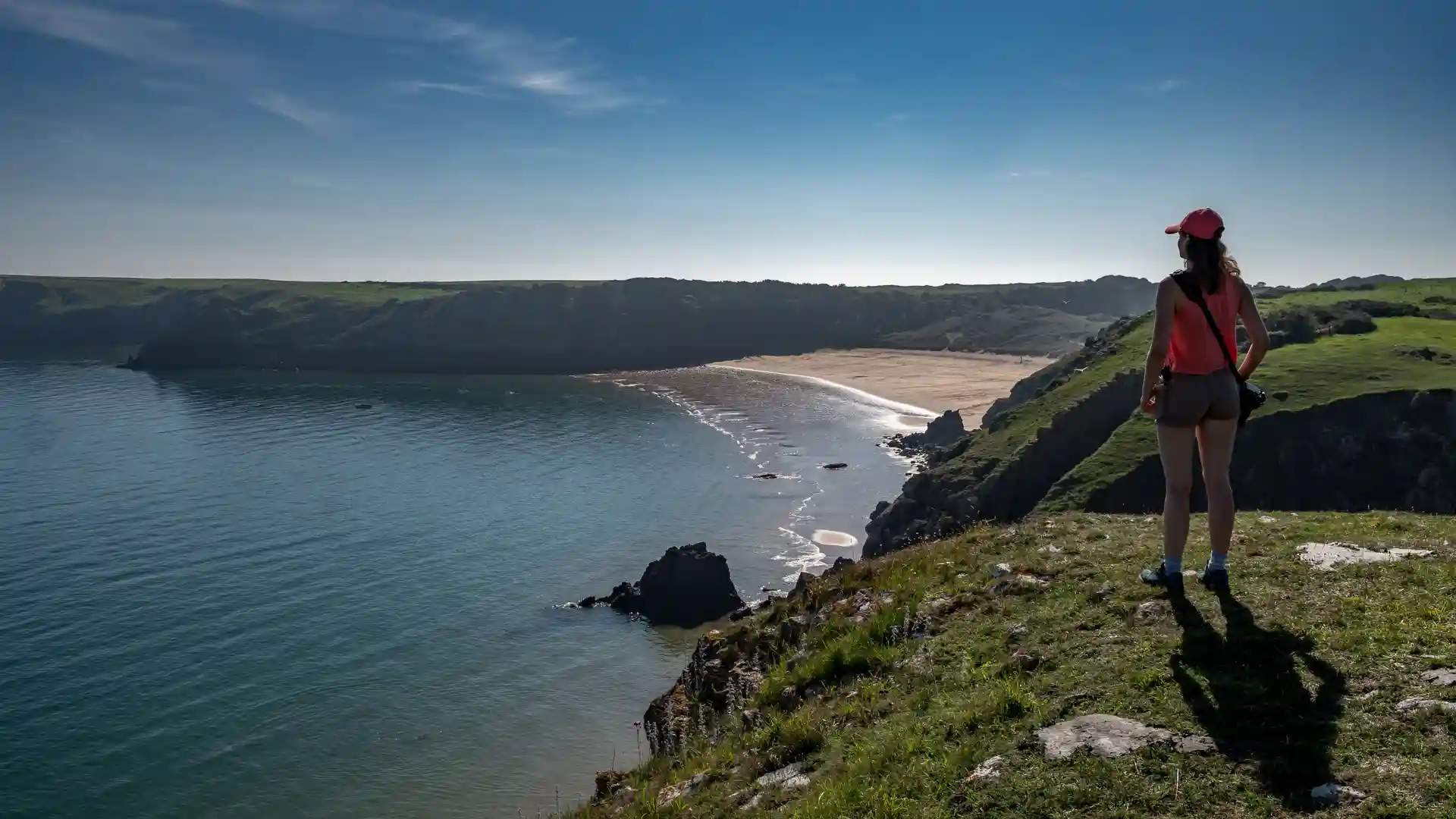 Walker on cliff-top above sandy bay on the Pembrokeshire Coast Path in Wales.
