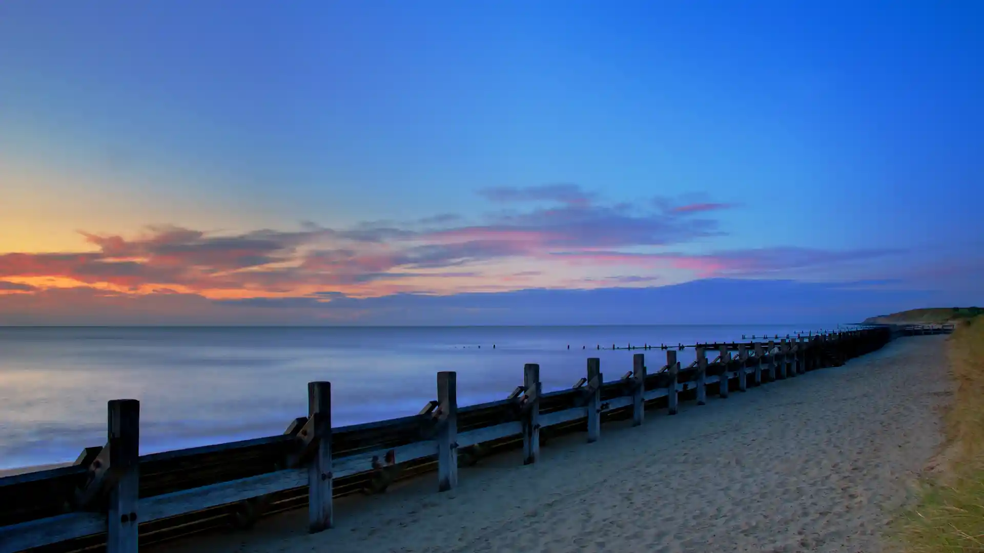 Sunset over the beach at Hopton-on-Sea with wooden groynes and calm sea, marking the end of the Norfolk Coast Path.