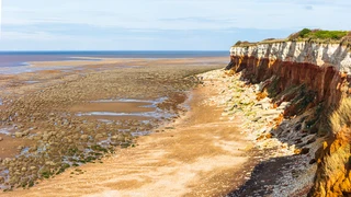 Hunstanton Cliffs on the Norfolk Coast Path showing red and white striped rock layers above a rocky shoreline at low tide.