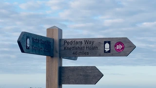 Wooden signpost on the Peddars Way at Knettishall Heath under an open sky, showing the exposed landscape and changing weather conditions along the route.