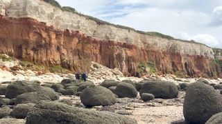 Walkers moving between large rock boulders beneath the striped cliffs at Hunstanton on the Norfolk Coast Path in Norfolk.