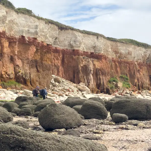 Walkers moving between large rock boulders beneath the striped cliffs at Hunstanton on the Norfolk Coast Path in Norfolk.