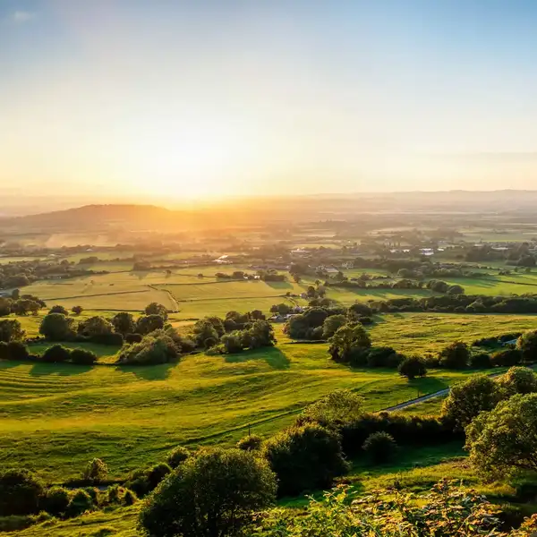 Rolling hills and patchwork farmland at sunset in the Cotswolds National Landscape.