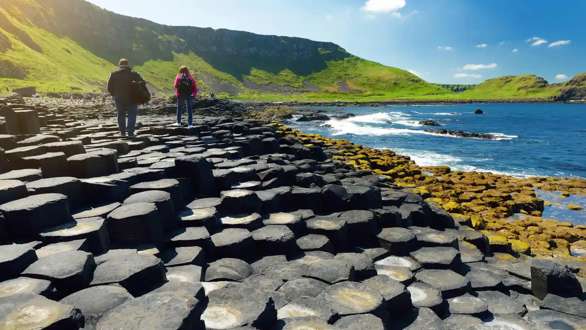 Walkers exploring the basalt columns of the Giant’s Causeway on a sunny day along Northern Ireland’s Causeway Coast.