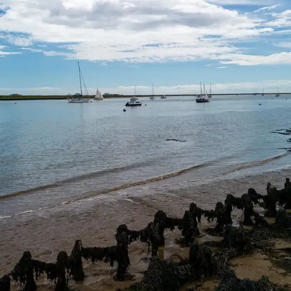 View across the River Ore estuary at Orford, with sailing boats, tidal mudflats, and saltmarsh along the Suffolk Coast Path.