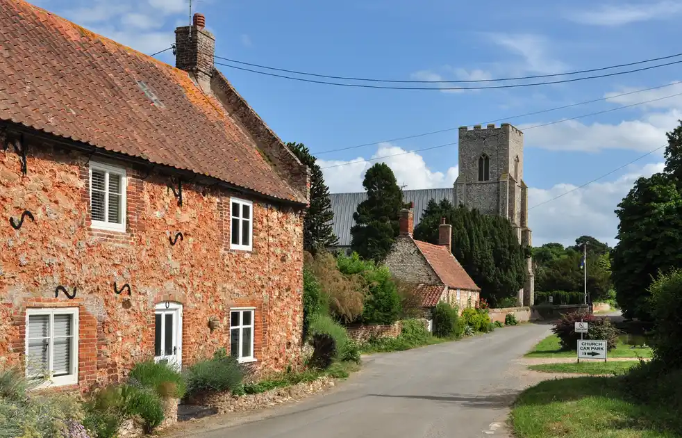 Old Hunstanton village street with traditional stone cottages and St Mary’s Church tower in the background.