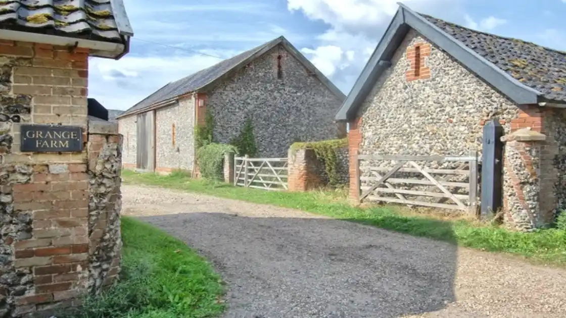 Grange Farm House, farm house entrance showing a shingle drive between flint built buildings. 
