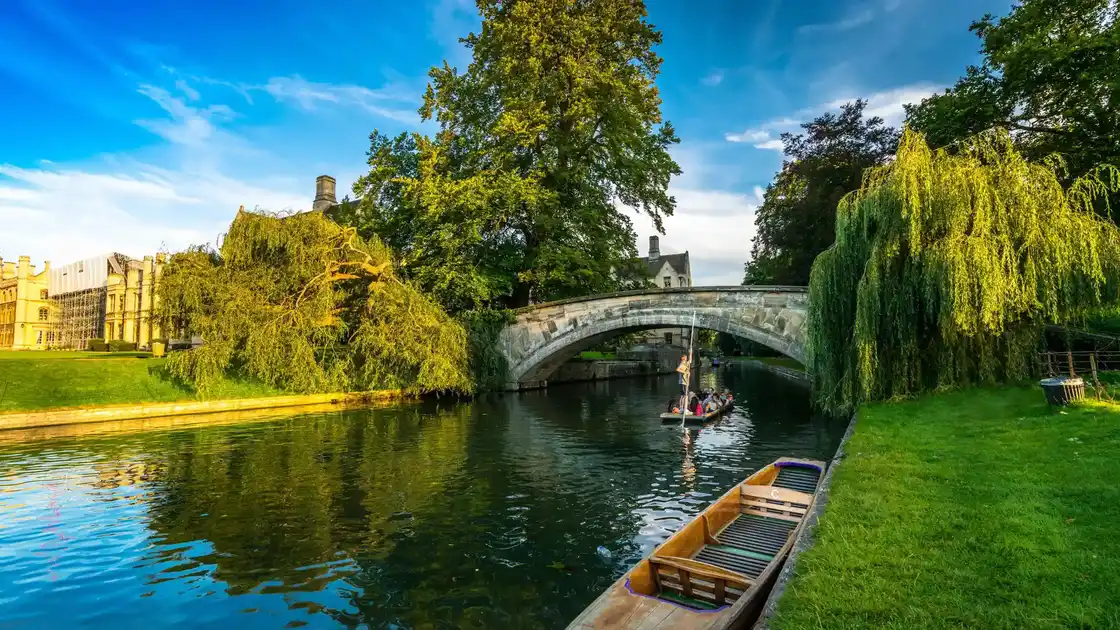 Boat full of people approach a low bridge on the canal of Cambridgeshire.