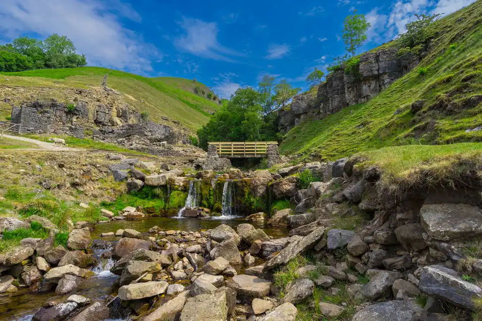 Swinner Gill in Swaledale, with a rocky stream, footbridge and limestone slopes in the Yorkshire Dales National Park.