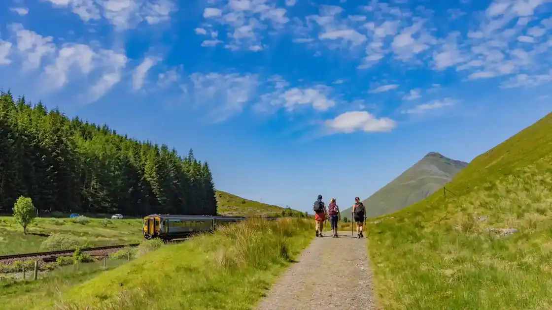 Walkers on the West Highland Way with train and Buachaille Etive Mòr in the Scottish Highlands.