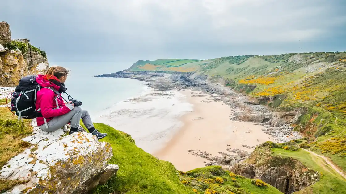 Walker overlooking Rhossili Bay from the Wales Coast Path on the Gower Peninsula, Wales.