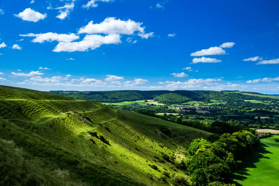 Rolling chalk downland overlooking a wooded valley, patchwork farmland and villages in Cranborne Chase National Landscape.