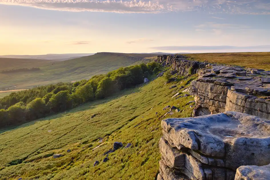 Gritstone cliffs at Stanage Edge overlooking wooded slopes and open moorland in the Peak District near Sheffield, South Yorkshire.