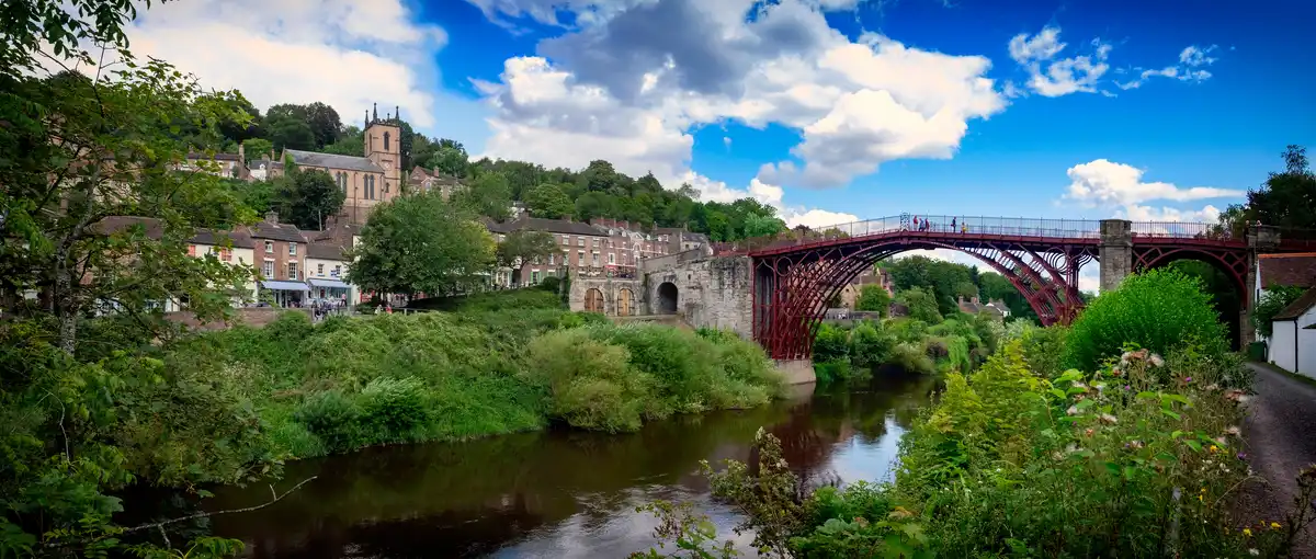 The historic Iron Bridge spanning the River Severn at Ironbridge Gorge in Shropshire, with wooded hills and the village beyond.