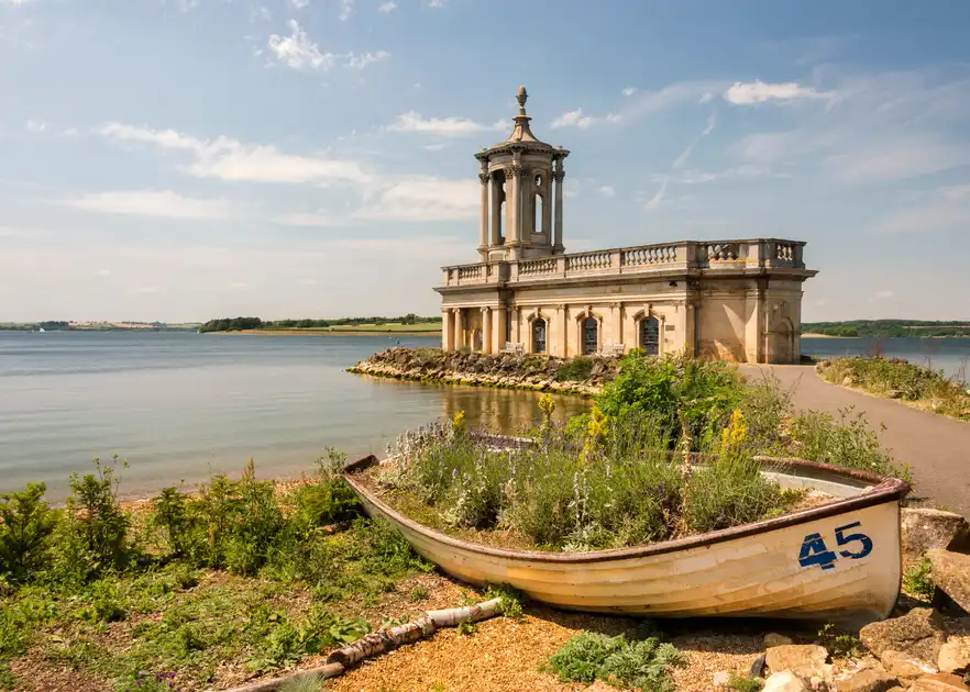 Normanton Church on the shores of Rutland Water in Rutland, with a small boat in the foreground and the reservoir stretching into the distance.