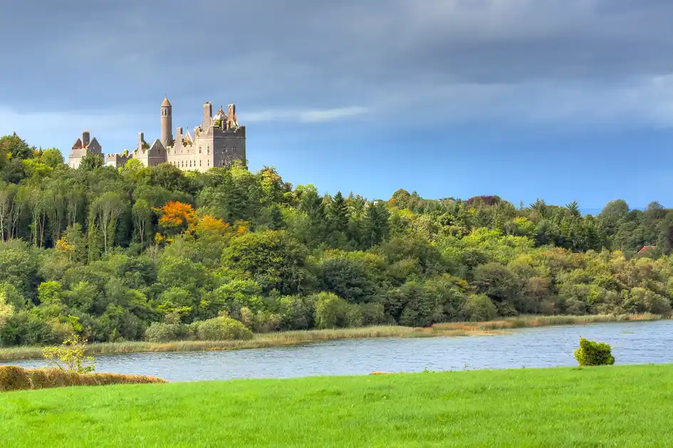 Dromore Castle overlooking a lake and surrounding woodland in County Limerick, Ireland, with green countryside in the foreground.