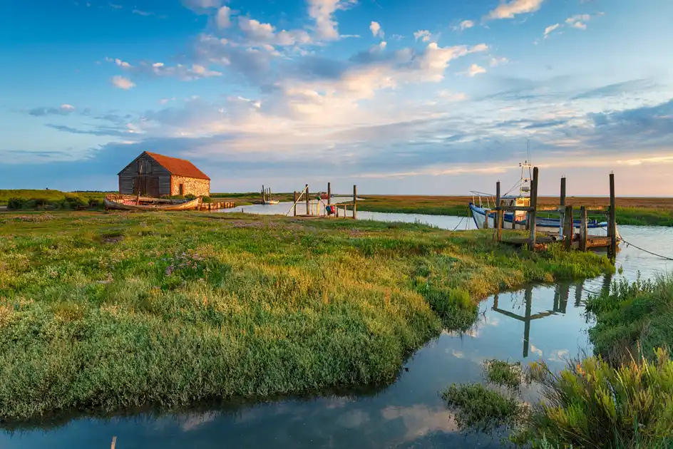 Fishing boats moored along a tidal creek at Thornham Harbour, surrounded by saltmarsh and a historic harbour building on the Norfolk coast.