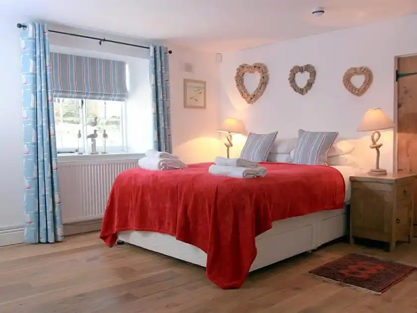 Guest bedroom at The Orange Tree in Thornham, Norfolk, with a double bed, red bedspread and wooden flooring.