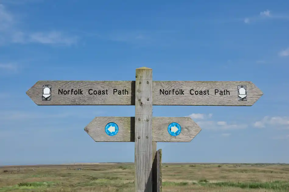 Wooden Norfolk Coast Path signpost pointing in both directions across open coastal marshland.