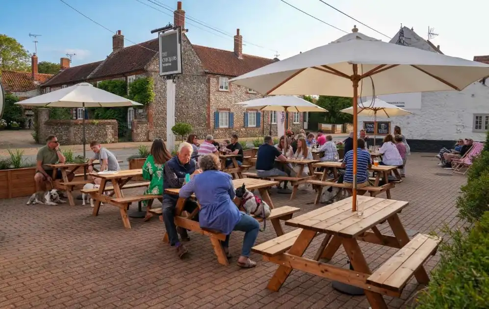 Guests enjoying outdoor dining at picnic tables beneath parasols in the courtyard of The Chequers Inn, Thornham, Norfolk.