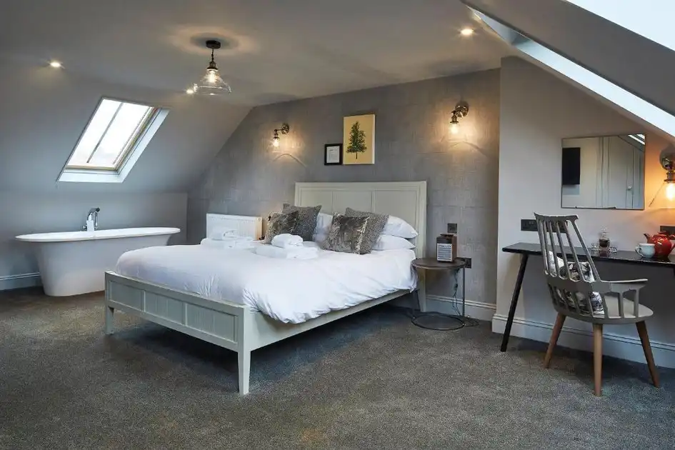 Guest bedroom at The Lifeboat Inn in Thornham, Norfolk, featuring a double bed, freestanding bathtub, skylight and writing desk.