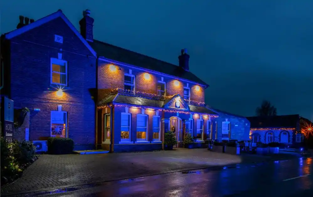 Exterior of Titchwell Manor Hotel in Titchwell, Norfolk, illuminated with blue and warm lighting at dusk.