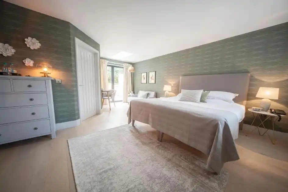 Contemporary guest bedroom at Titchwell Manor Hotel in Titchwell, Norfolk, featuring a king-size bed, soft grey furnishings and French doors opening towards the garden.