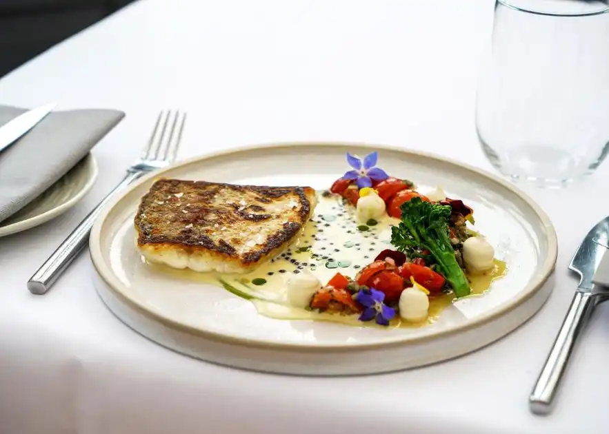 Restaurant dish at Titchwell Manor Hotel in Titchwell, Norfolk, featuring pan-fried fish with seasonal vegetables, creamy sauce and edible flowers.