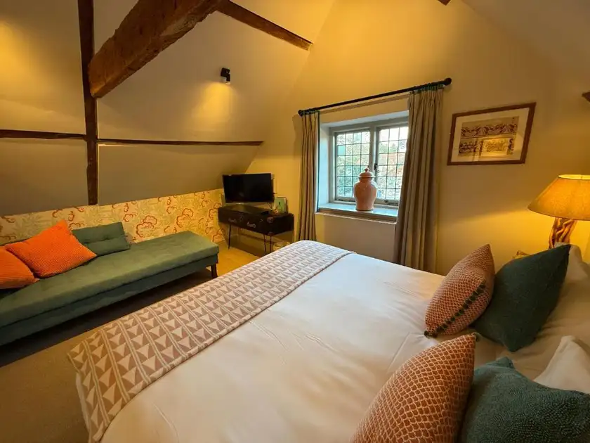 Guest bedroom at The Ship in Brancaster, Norfolk, featuring exposed wooden beams, a double bed, upholstered sofa and traditional leaded window.
