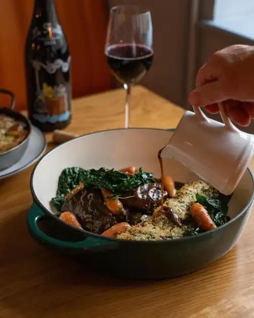 Restaurant dish at The Ship in Brancaster, Norfolk, featuring slow-cooked meat with carrots and greens, with sauce being poured over the food.