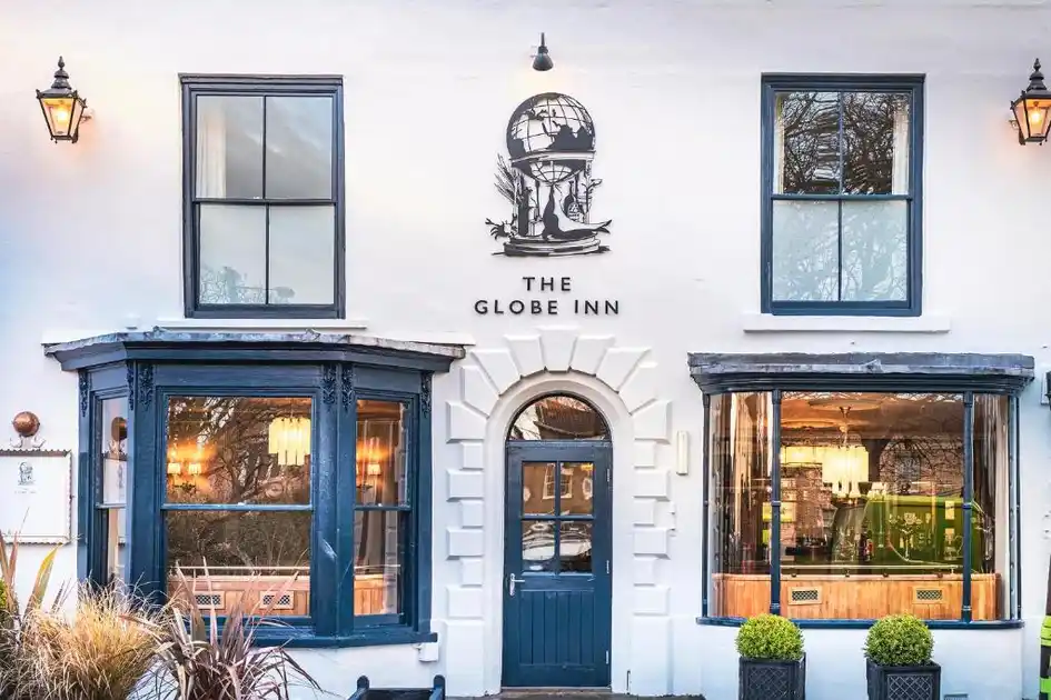 Exterior of The Globe Inn in Wells-next-the-Sea, Norfolk, showing the whitewashed façade, blue-painted entrance and bay windows, with the inn's distinctive globe sign above the doorway.