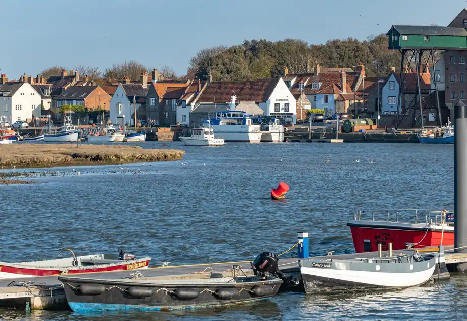 Fishing boats and pleasure craft moored in Wells-next-the-Sea Harbour, Norfolk, with the historic brick granary and waterfront buildings overlooking the quay.