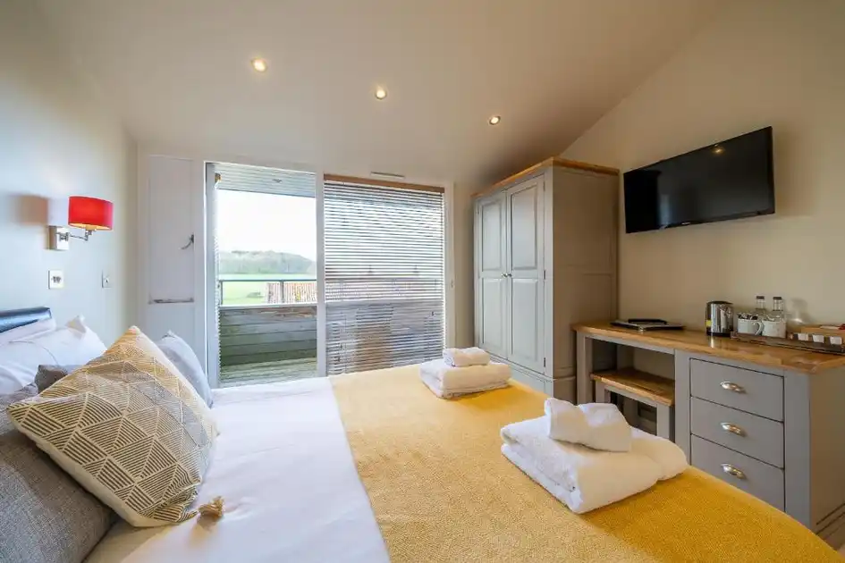 Guest bedroom at The Red Lion in Stiffkey, Norfolk, featuring a double bed, yellow bedspread, modern furnishings, television and glass doors opening onto a private balcony with countryside views.