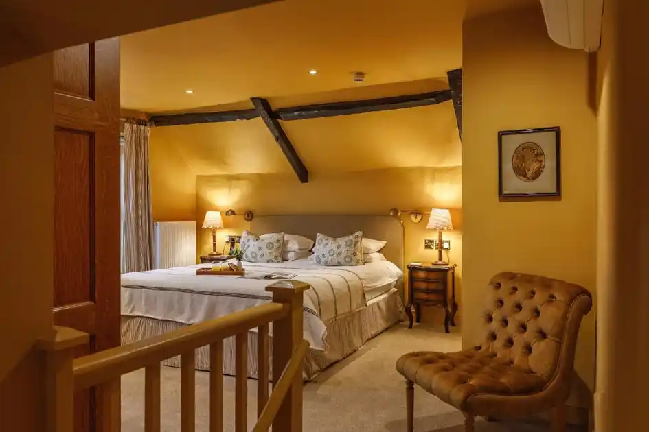 Guest bedroom at Morston Hall in Morston, Norfolk, featuring a double bed with patterned cushions, exposed wooden ceiling beams, bedside lamps and a tufted armchair.