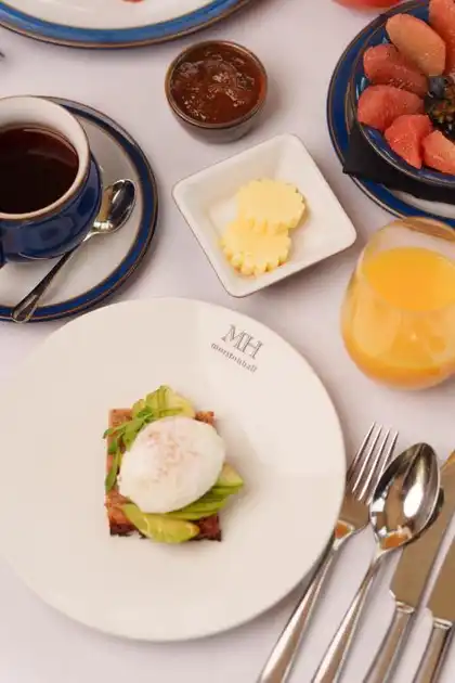 Breakfast at Morston Hall in Morston, Norfolk, featuring a poached egg on toast with avocado, fresh fruit, orange juice, tea and preserves on a white tablecloth.