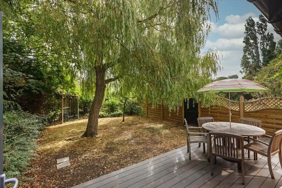 Private garden terrace at Morston Hall in Morston, Norfolk, featuring wooden outdoor furniture, a parasol and a mature willow tree overlooking a secluded garden.
