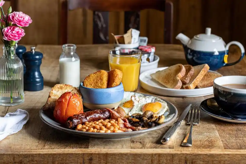 Full English breakfast served at Three Swallows in Cley-next-the-Sea, Norfolk, featuring bacon, sausage, fried egg, baked beans, mushrooms, grilled tomato and hash browns, with toast, orange juice and tea.