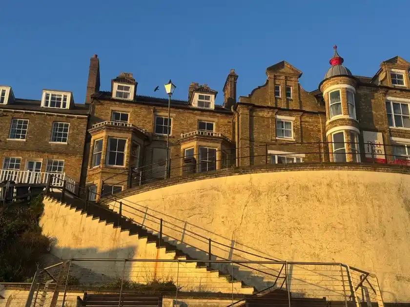 Seafront exterior of The Red Lion Hotel in Cromer, Norfolk, showing its historic brick façade, bay windows, distinctive turret and steps leading up from the promenade.